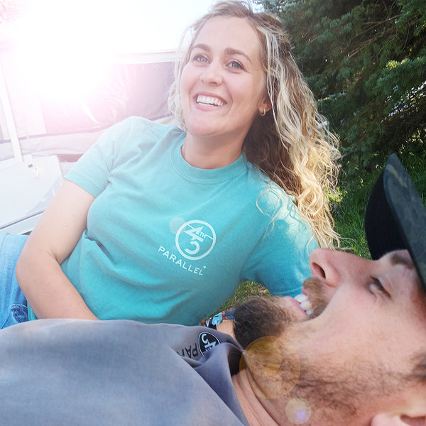 Woman wearing 45th Parallel Puff Ink Activity Tee in Sea Foam Blue, smiling outdoors with a man beside her, enjoying a sunny day.