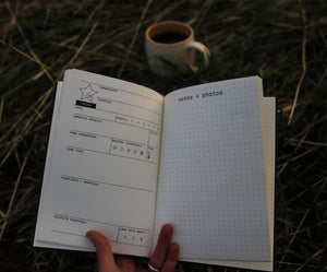 45th Parallel Basecamp Journal open to campsite log pages with coffee mug in background