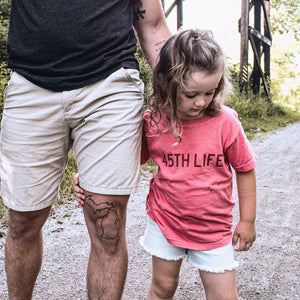 Toddler wearing a pink 45th Parallel tee walking a trail with an adult