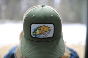 45th Parallel Trout Patch Trucker hat with trout illustration in outdoor setting